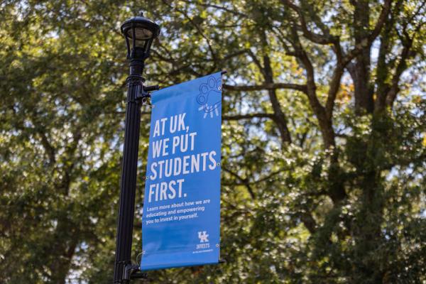 A UK Invests banner hanging from a light pole over a walkway on campus.